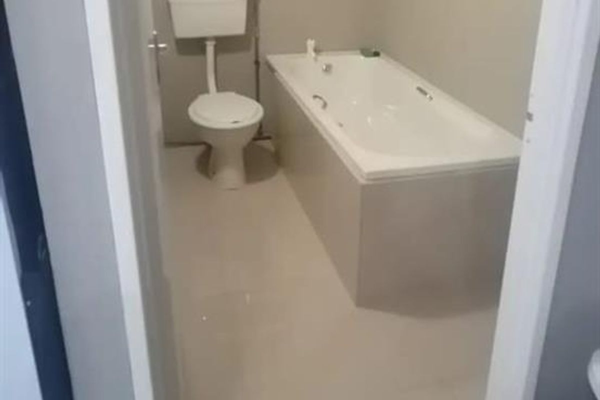 A functional bathroom featuring a built-in bathtub, a standard toilet, and a window with security bars.