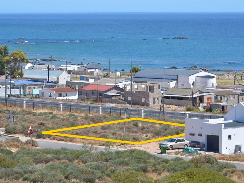 An elevated view of a vacant residential plot marked with a yellow boundary, situated in a coastal neighborhood with ocean views.