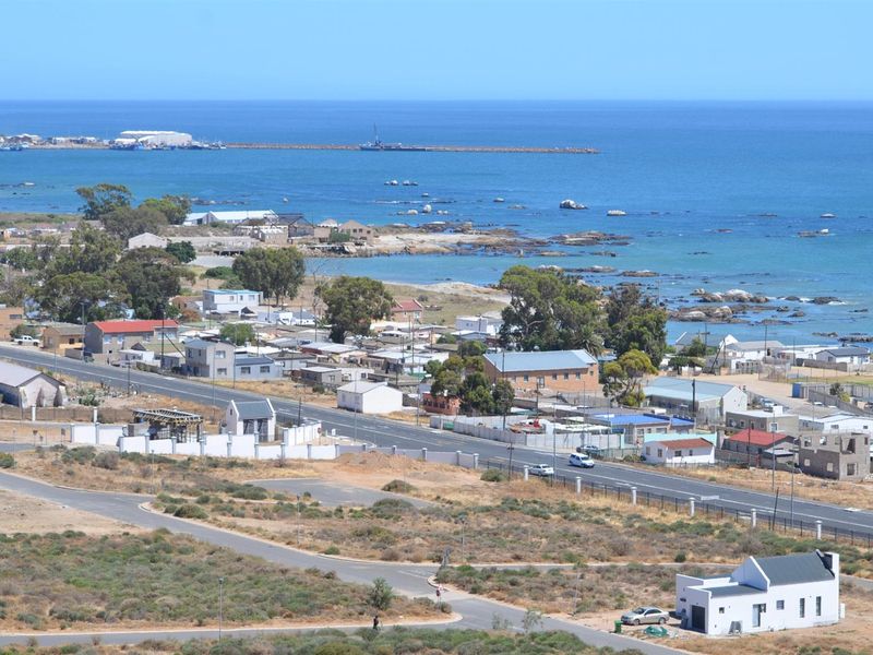 An elevated aerial view of the coastal residential area, showcasing the surrounding landscape, nearby road infrastructure, and proximity to the ocean.