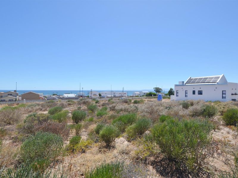 A vacant residential plot featuring natural coastal vegetation, offering a clear view of the surrounding neighborhood and the nearby ocean.
