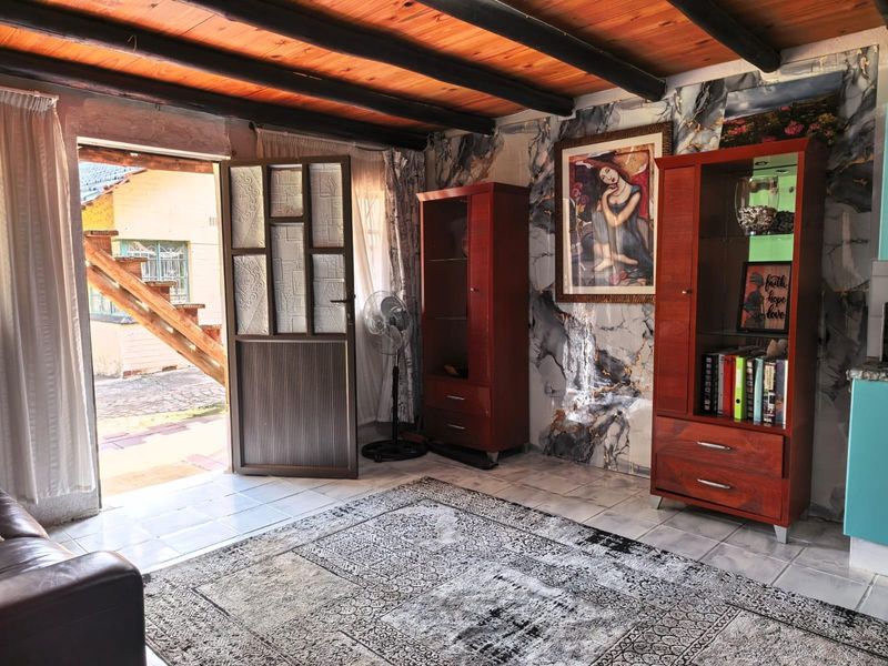 Living area featuring exposed timber ceiling beams, tiled flooring, and a decorative marble-effect feature wall with direct access to the exterior.