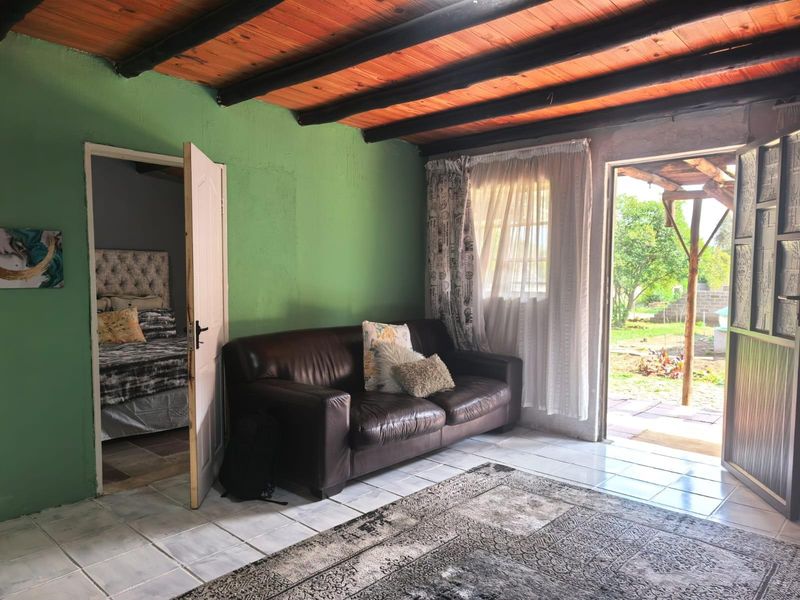 Living room featuring exposed timber ceiling beams, tiled flooring, and direct access to both a bedroom and the outdoor garden area.