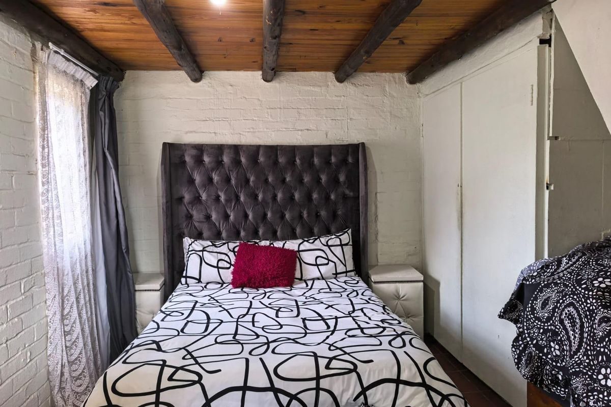 A cozy bedroom featuring exposed timber ceiling beams, painted brick walls, and a built-in wardrobe.