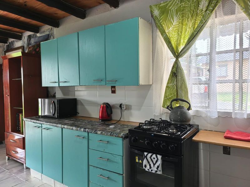 A functional kitchen featuring turquoise cabinetry, a gas stove with oven, tiled backsplash, and exposed timber ceiling beams.