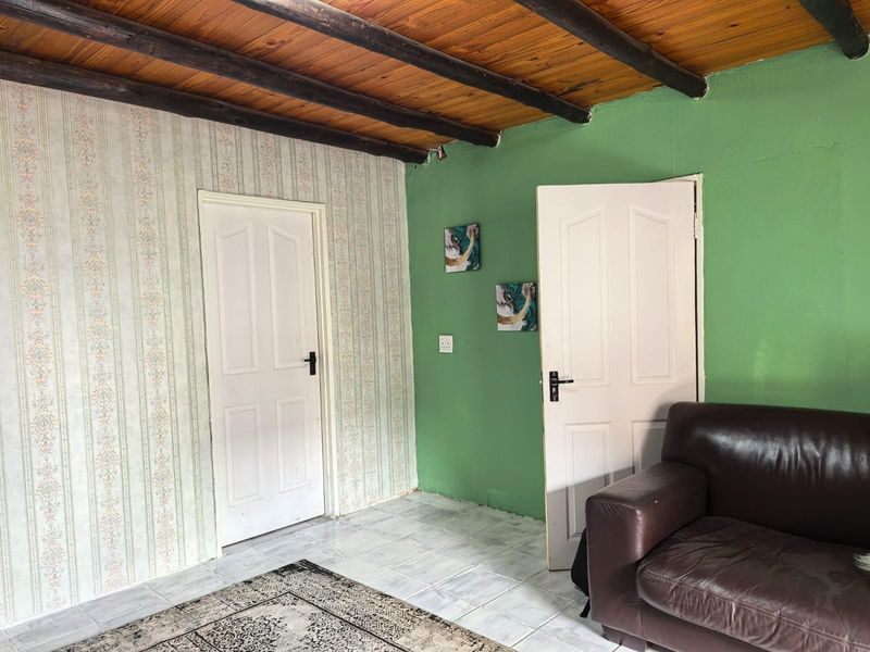 Living area featuring exposed timber beam ceilings, tiled flooring, and dual access doors with dated wallpaper and painted wall finishes.