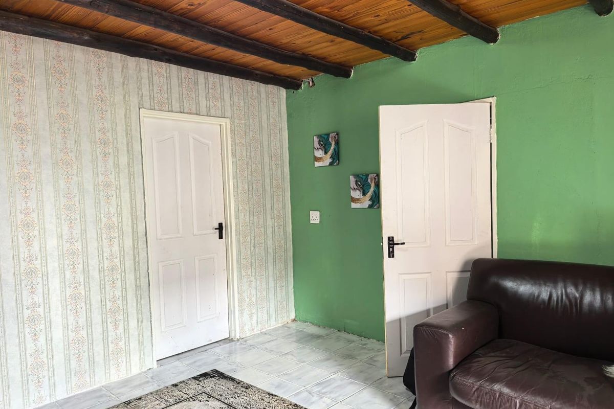 Living area featuring exposed timber beam ceilings, tiled flooring, and dual access doors with dated wallpaper and painted wall finishes.
