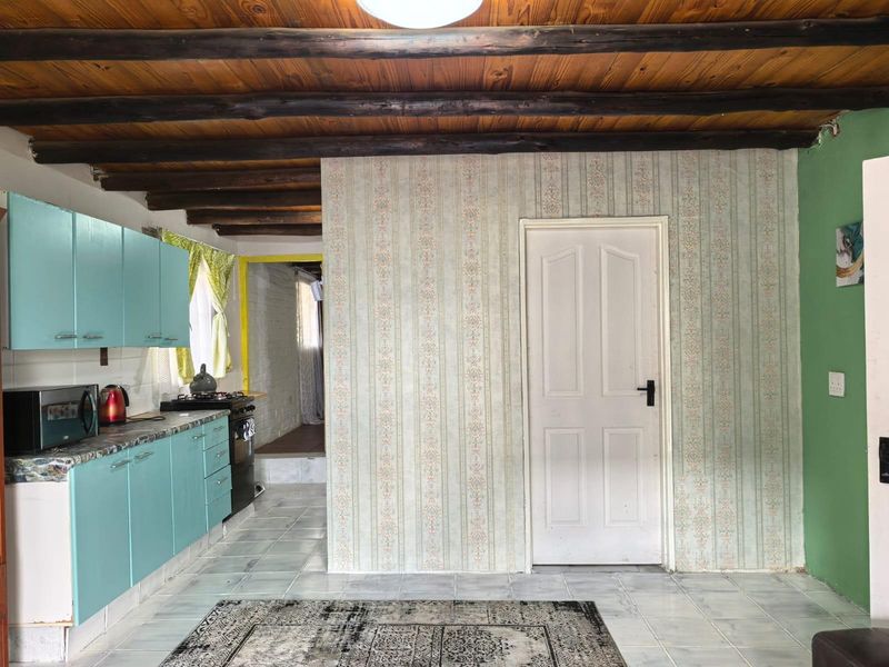 A kitchen area featuring exposed timber ceiling beams, tiled flooring, and dated cabinetry, offering potential for a modern renovation.