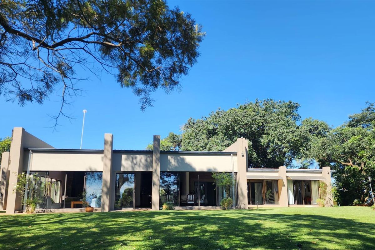 A well-maintained rear elevation of the property featuring large glass sliding doors, covered patio areas, and expansive manicured lawn gardens.