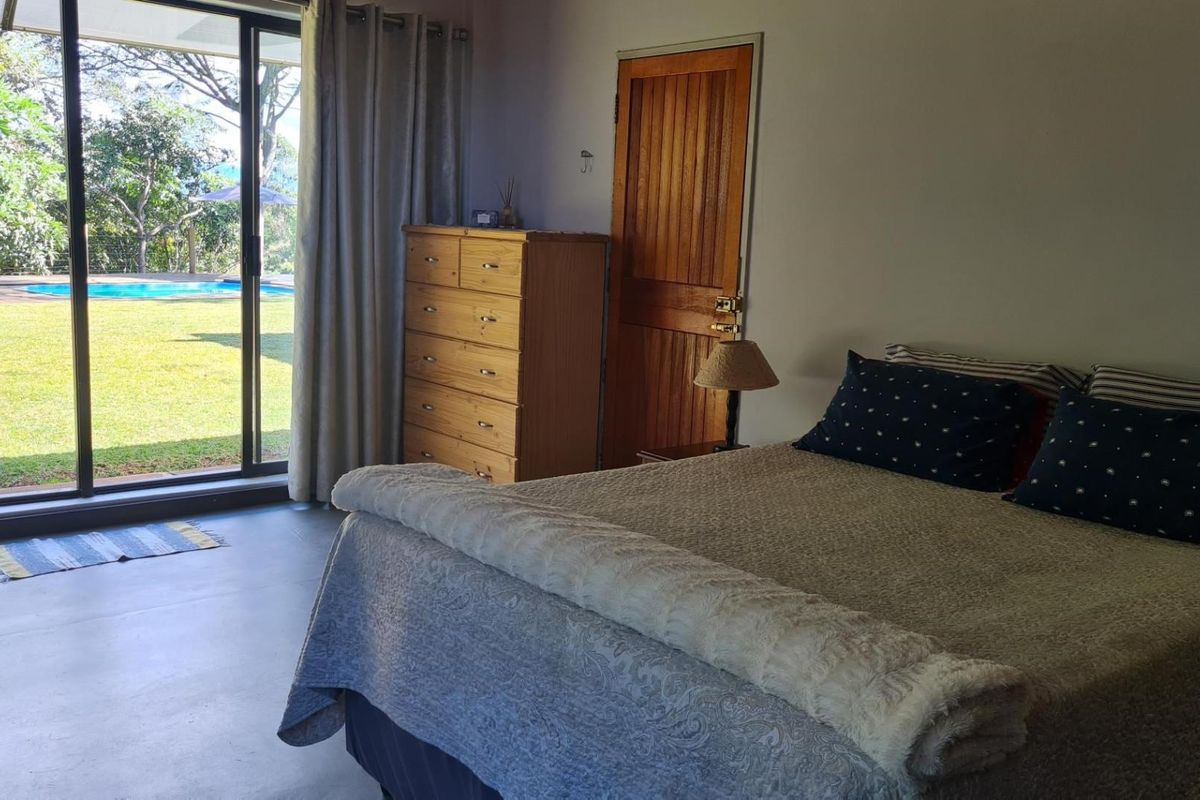 A bedroom featuring polished concrete flooring and large sliding glass doors that provide direct access to the garden and pool area.