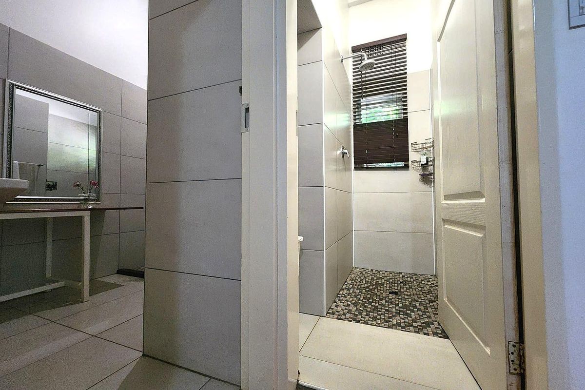 A modern bathroom featuring a walk-in shower with mosaic tile flooring, large format wall tiles, and a vanity area with a mirror.