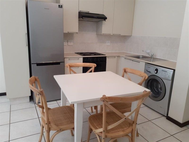 Compact kitchen featuring built-in cabinetry, laminate countertops, a stainless steel sink, and integrated cooking appliances with tiled flooring and backsplash.