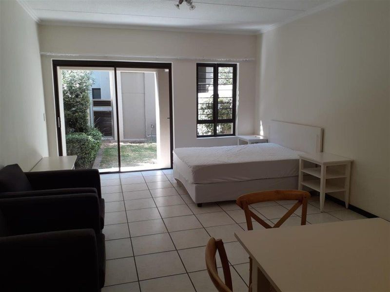 Open plan living and sleeping area featuring tiled floors, large sliding glass doors providing garden access, and natural light through a window with security bars.