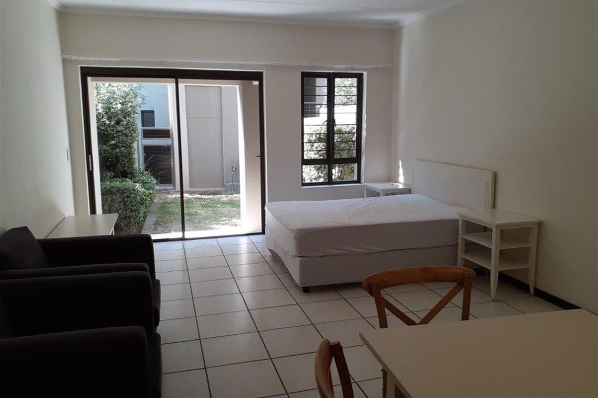 Open plan living and sleeping area featuring tiled floors, large sliding glass doors providing garden access, and natural light through a window with security bars.