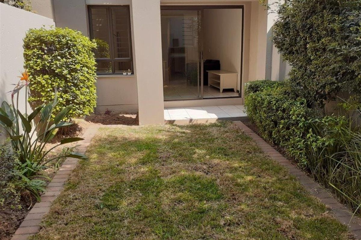 A private rear garden area featuring a small lawn with paved borders and a sliding glass door providing access to the apartment interior.