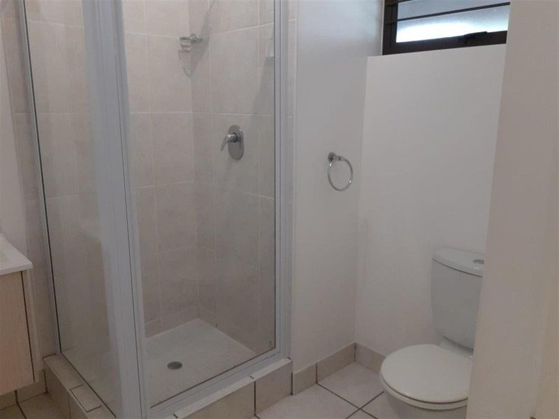 A clean, functional bathroom featuring a glass-enclosed shower, a standard toilet, and a vanity cabinet with tiled finishes throughout.