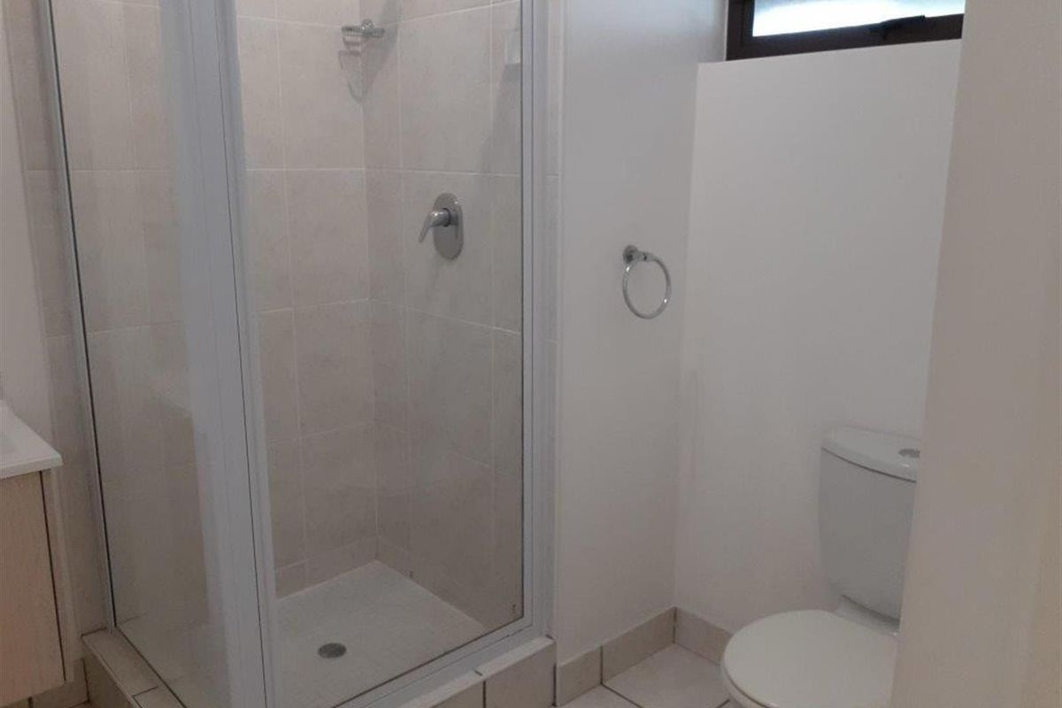 A clean, functional bathroom featuring a glass-enclosed shower, a standard toilet, and a vanity cabinet with tiled finishes throughout.