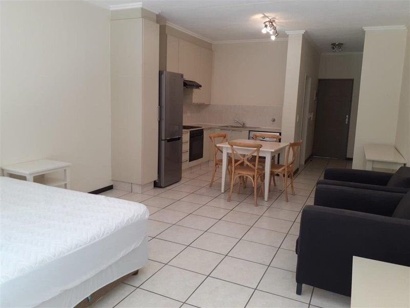 Open-plan apartment living area featuring a functional kitchen with built-in cabinetry, oven, hob, and tiled flooring throughout.