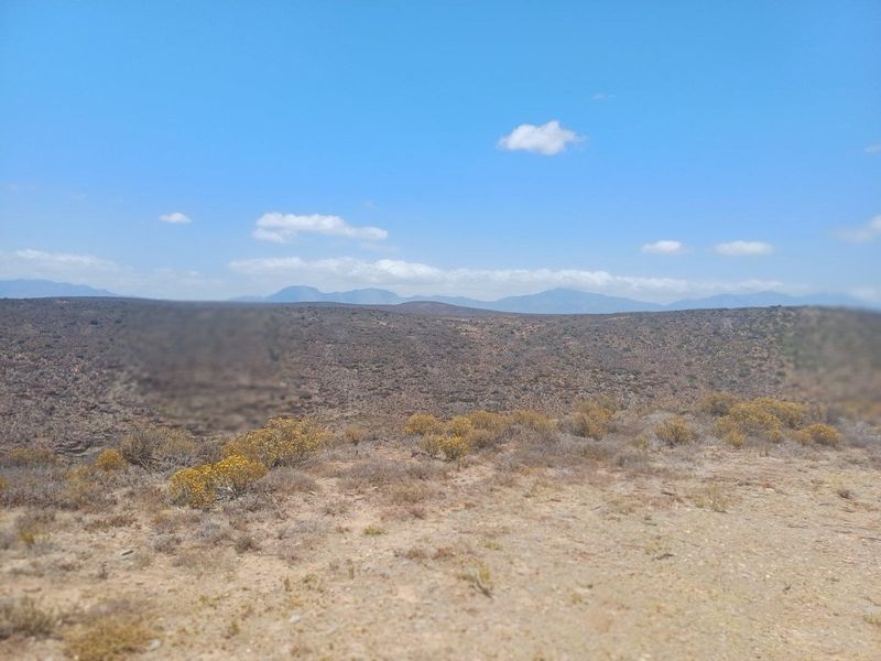 Expansive landscape view overlooking arid farm terrain with distant mountain ranges under a clear blue sky.