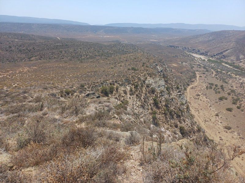 Expansive panoramic view of the rugged farm landscape, featuring natural rocky terrain, dry riverbeds, and distant mountain ranges.