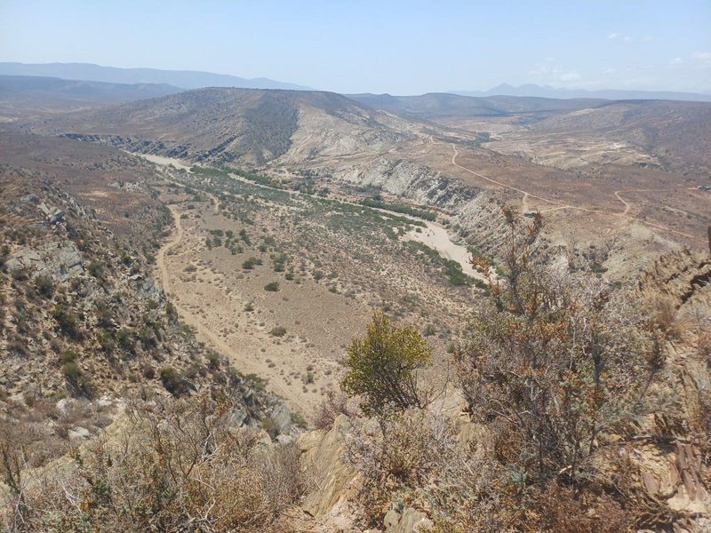 Expansive elevated landscape view overlooking a rugged valley, dry riverbed, and surrounding mountainous terrain on the farm property.