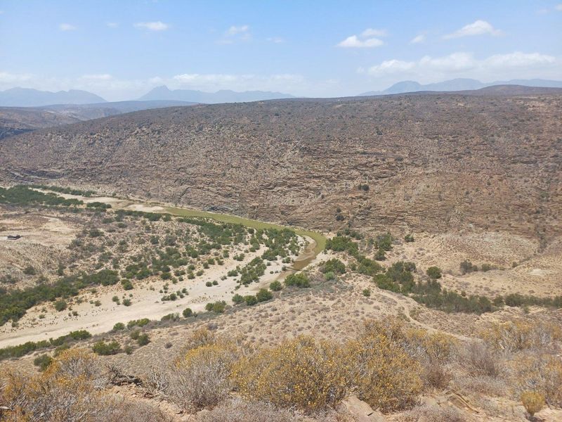 A scenic elevated view of the expansive arid landscape, featuring a winding riverbed through the valley and distant mountain ranges.
