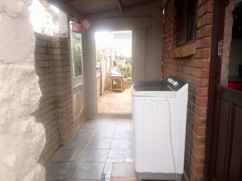 A functional outdoor laundry area featuring tiled flooring and exposed brick walls, providing direct access to the rear garden space.