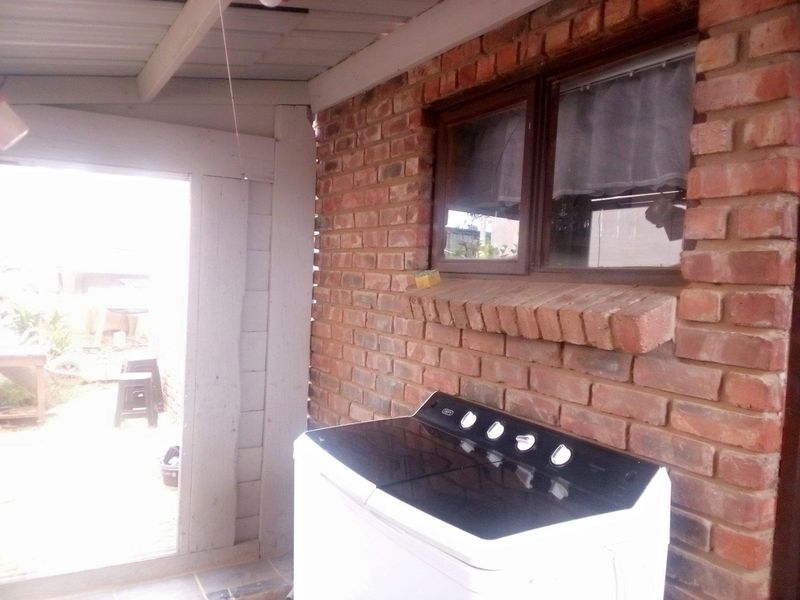 A functional laundry area featuring exposed brick walls and tiled flooring, situated under a covered outdoor structure.