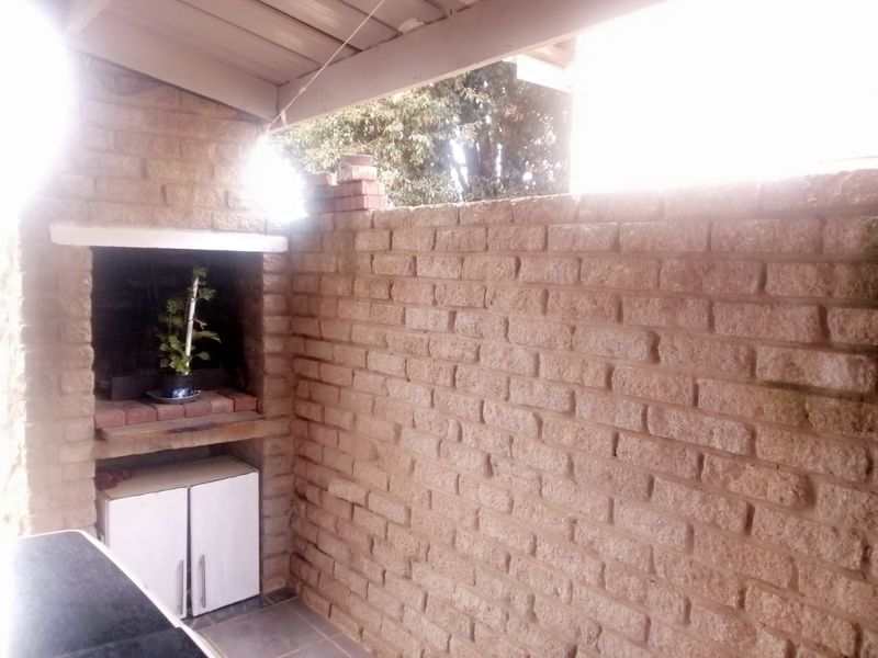 A covered outdoor patio area featuring a built-in brick braai and rustic brick wall finishes, providing a functional space for outdoor entertaining.