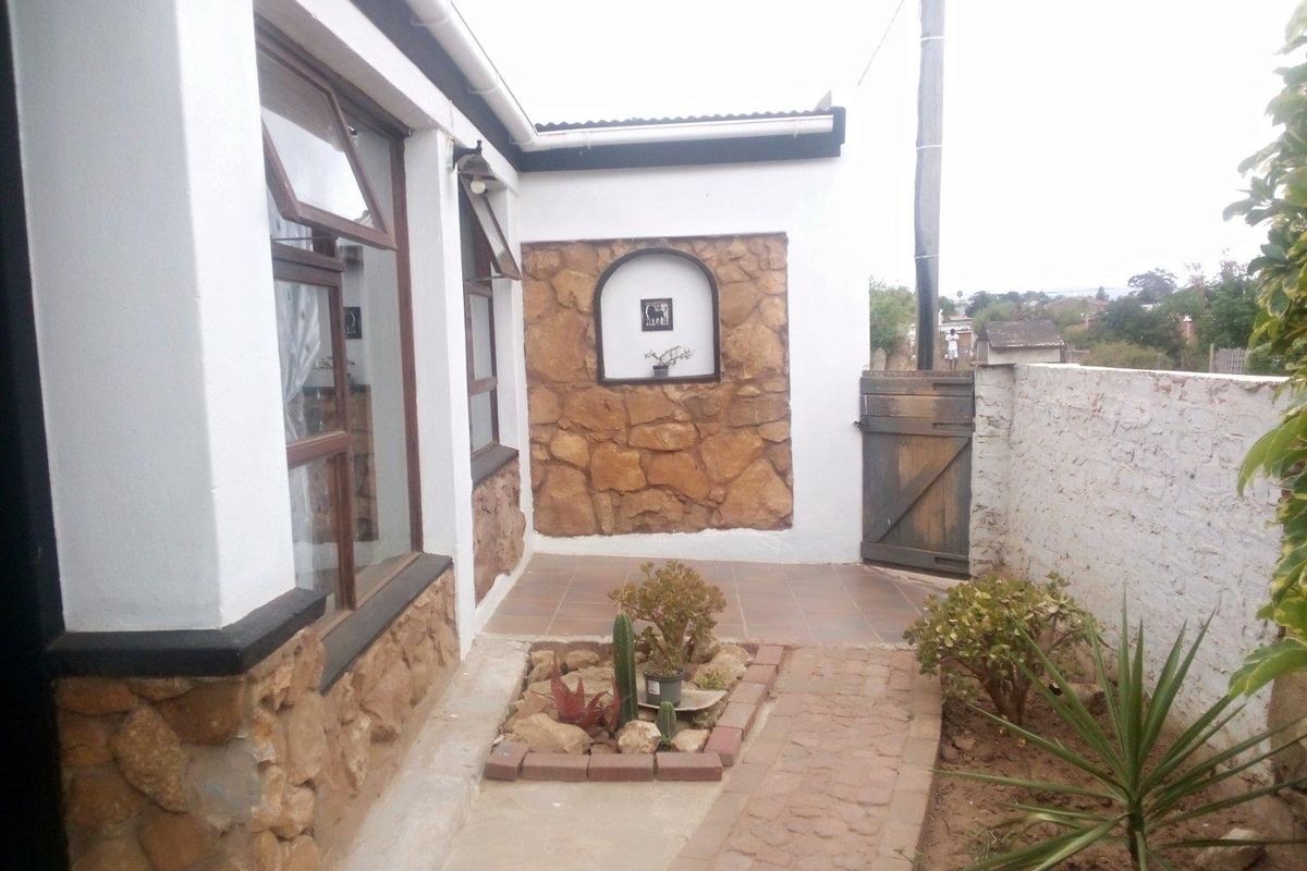 A rear courtyard area featuring stone-clad exterior walls, a tiled patio section, and a brick-paved pathway leading to a timber gate.