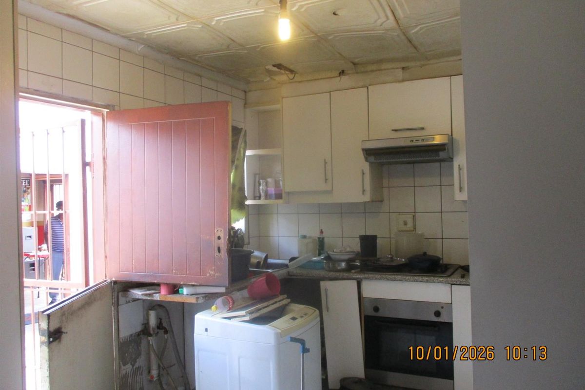 A compact kitchen featuring built-in cabinetry, an integrated oven and extractor fan, tiled splashbacks, and direct access to an outdoor area.