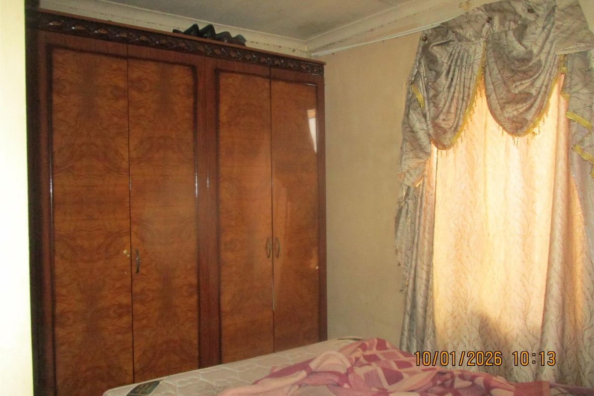 A bedroom featuring built-in wooden cabinetry and a window with decorative curtains, showing signs of wear and requiring cosmetic updates.