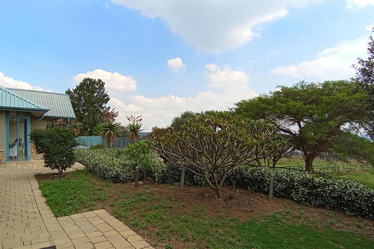 A view of the rear garden featuring paved walkways, established landscaping, and a metal roof structure on the adjacent building.