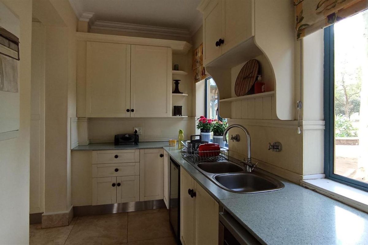 A functional kitchen featuring cream-colored cabinetry, stone-look countertops, a double stainless steel sink, and large windows providing natural light and garden views.