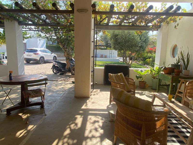A covered patio area featuring a rustic timber pergola, concrete flooring, and direct access to the garden and driveway.