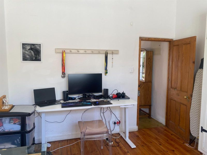 A functional home office space featuring polished wooden flooring and a classic timber door leading to an adjacent room.