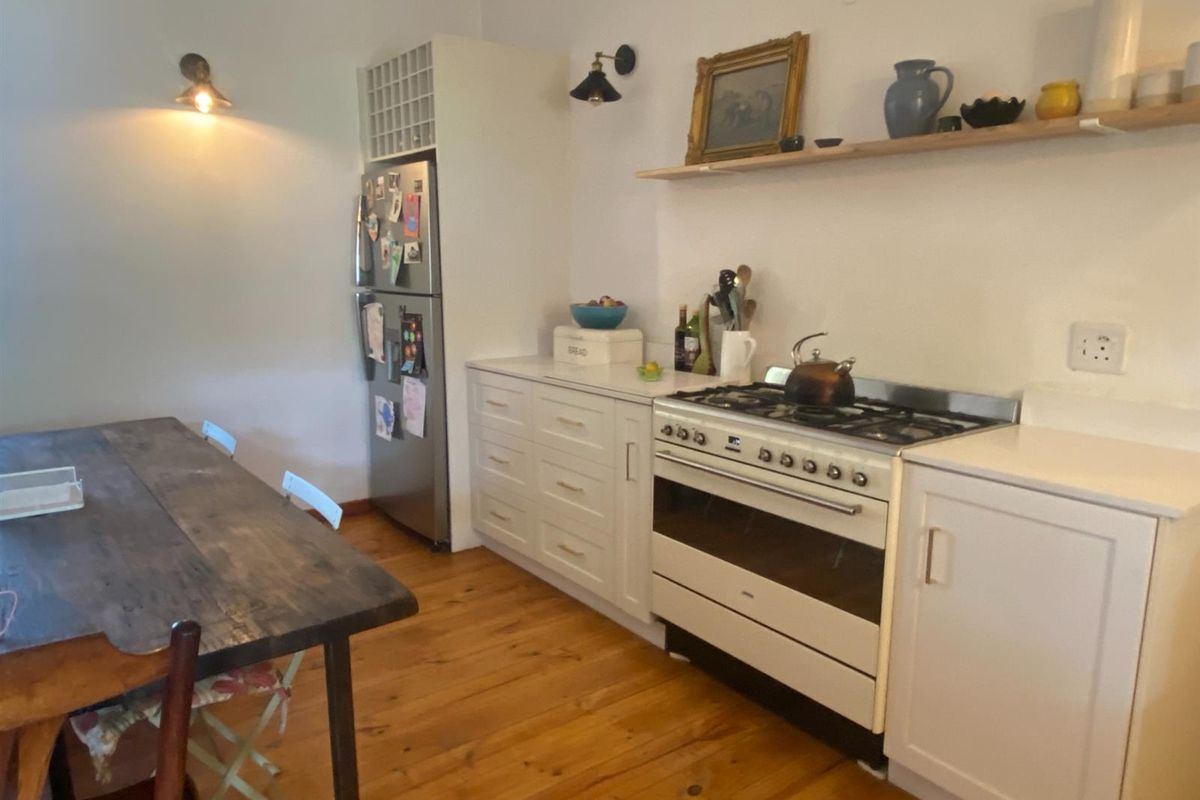 A functional kitchen featuring white cabinetry, a gas stove with oven, and warm timber flooring, creating a cozy and practical cooking space.