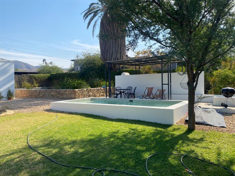 Outdoor pool area featuring a raised concrete swimming pool, a covered patio structure, and landscaped garden surroundings.