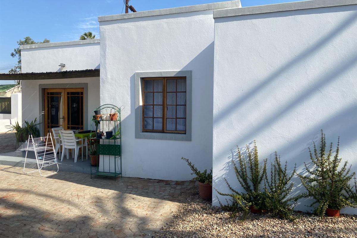 A view of the rear exterior facade featuring white plastered walls, timber-framed windows, and a paved patio area.