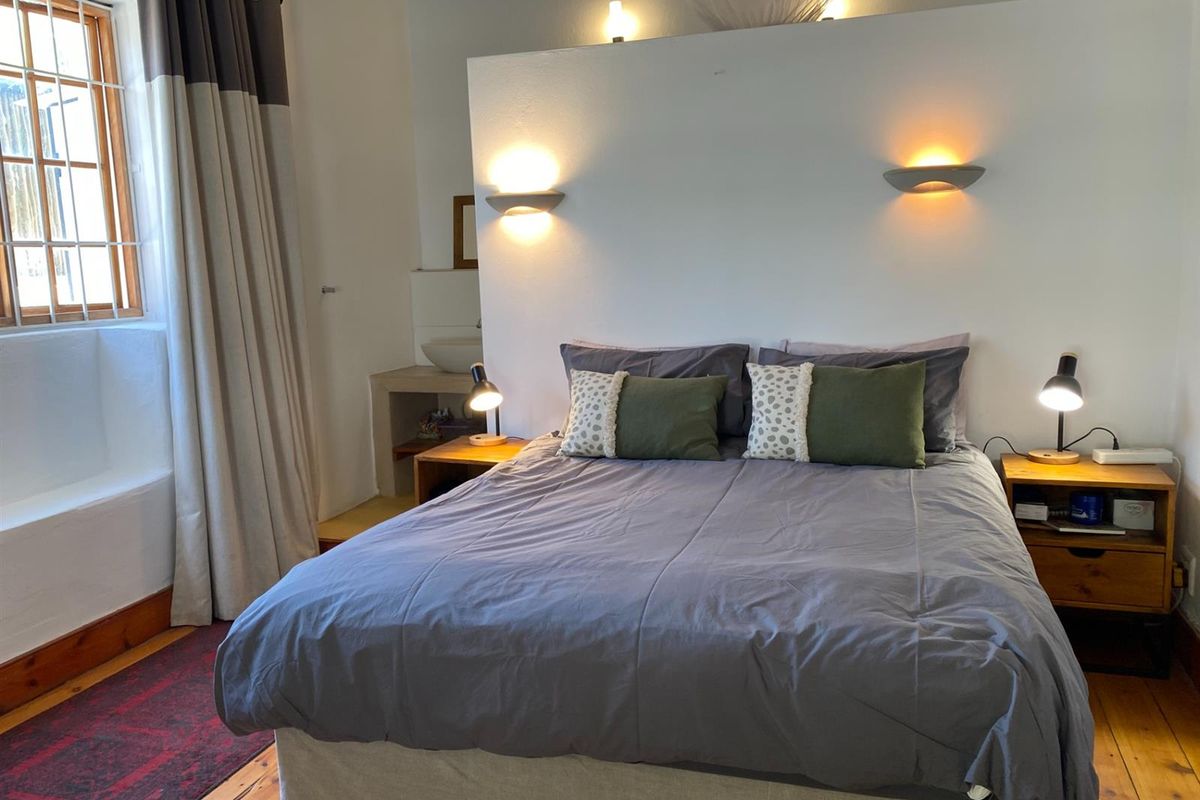 A cozy bedroom featuring a central partition wall with integrated wall lighting, timber flooring, and a built-in vanity area.