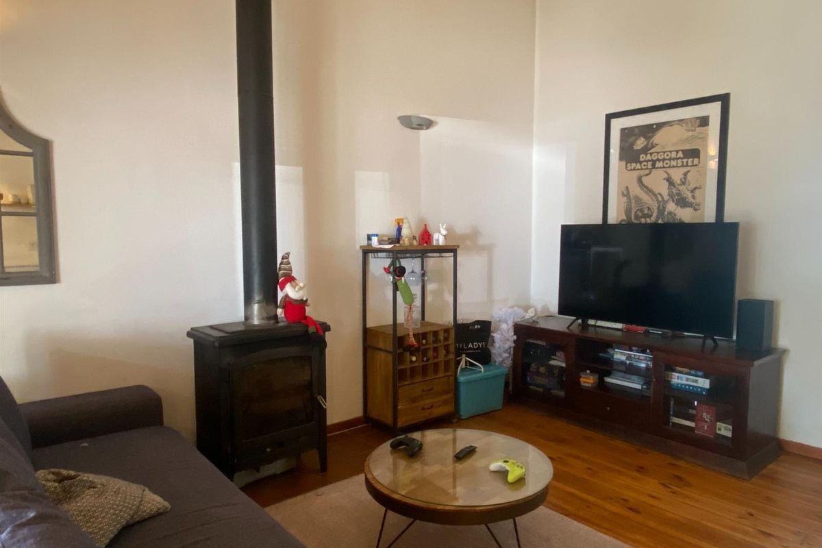 A cozy living room featuring polished timber flooring and a prominent black cast-iron wood-burning fireplace with a vertical flue.