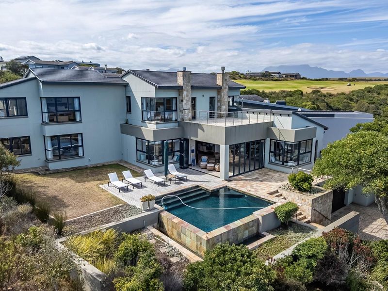 Aerial view of a modern multi-story residence featuring a swimming pool, stone-clad accents, expansive decking, and a balcony overlooking the surrounding landscape.