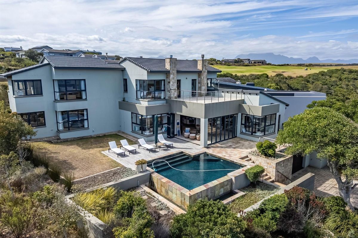 Aerial view of a modern multi-story residence featuring a swimming pool, stone-clad accents, expansive decking, and a balcony overlooking the surrounding landscape.