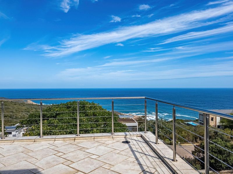 Spacious elevated balcony featuring stone tiling and a modern stainless steel balustrade, offering expansive, unobstructed ocean views.