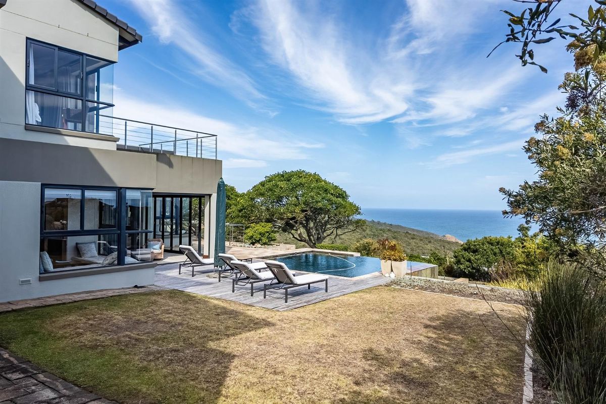Rear exterior view featuring a swimming pool, timber deck, and balcony overlooking the ocean with expansive coastal views.