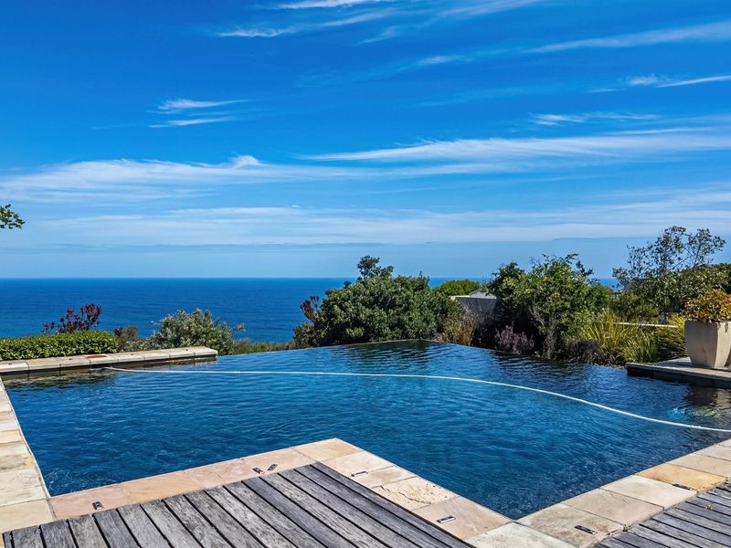 An infinity edge swimming pool featuring stone coping and timber decking, offering expansive ocean views.
