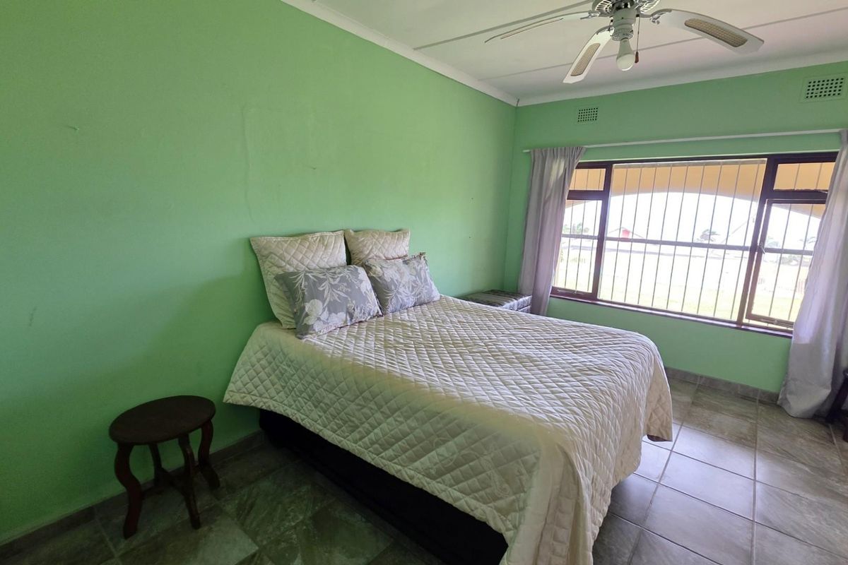 A bedroom featuring tiled flooring, a ceiling fan, and large windows with security bars, providing natural light and a view of the exterior.