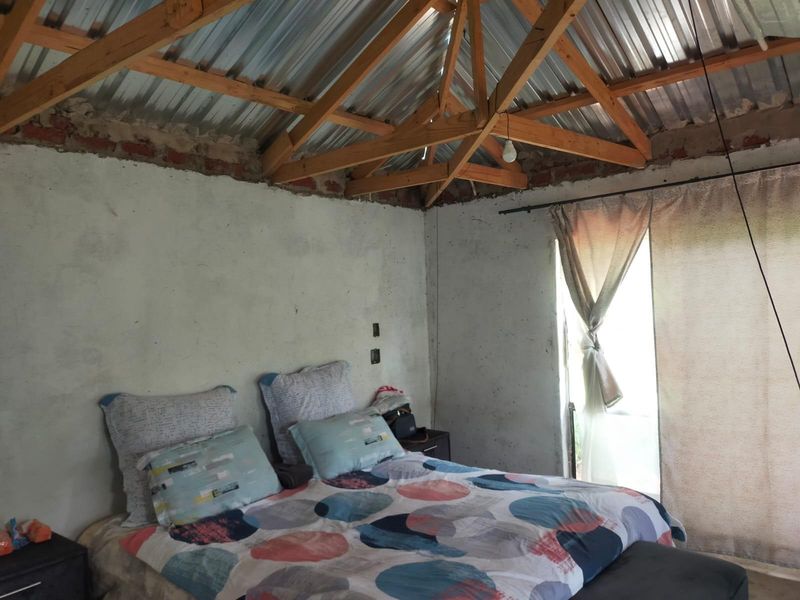 A bedroom featuring exposed timber roof trusses and corrugated metal roofing, with unfinished wall surfaces requiring plastering and finishing.