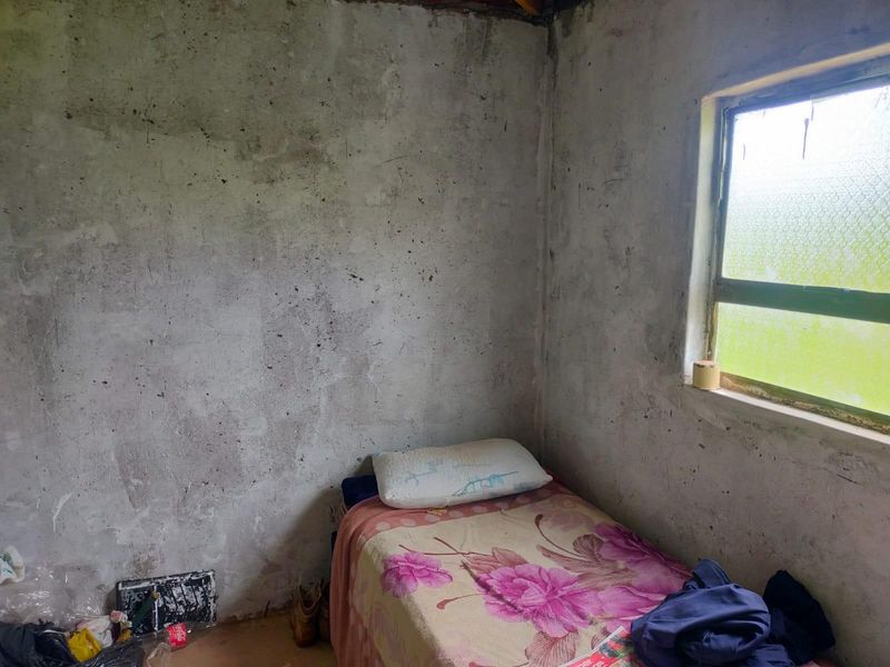 A small bedroom featuring unfinished concrete walls and a single window, requiring significant renovation and cosmetic updates to improve the living space.