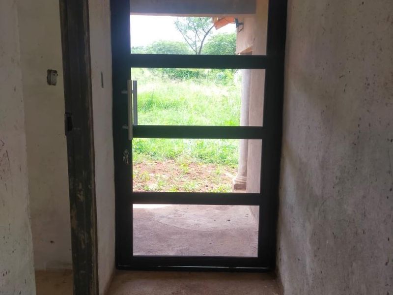 An unfinished entry area featuring a modern metal-framed glass door, exposed masonry walls, and concrete flooring, awaiting final plastering and finishing.