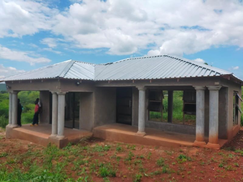 A single-story house under construction featuring a corrugated metal roof, concrete columns, and an open veranda, currently in an unfinished state.